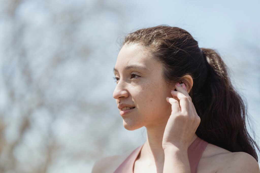 Young woman with earbuds enjoying a sunny day outdoors, making eye contact.